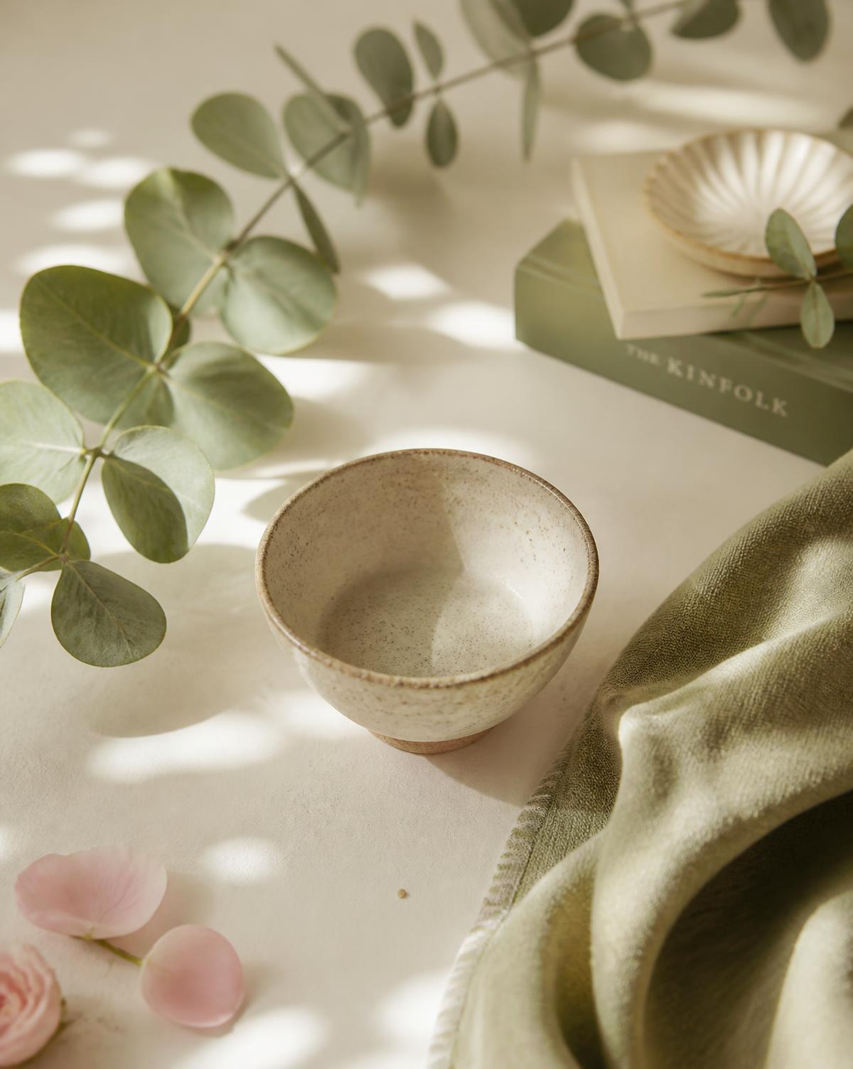 A calming still life of eucalyptus, a ceramic bowl and soft linen in warm sage and cream tones