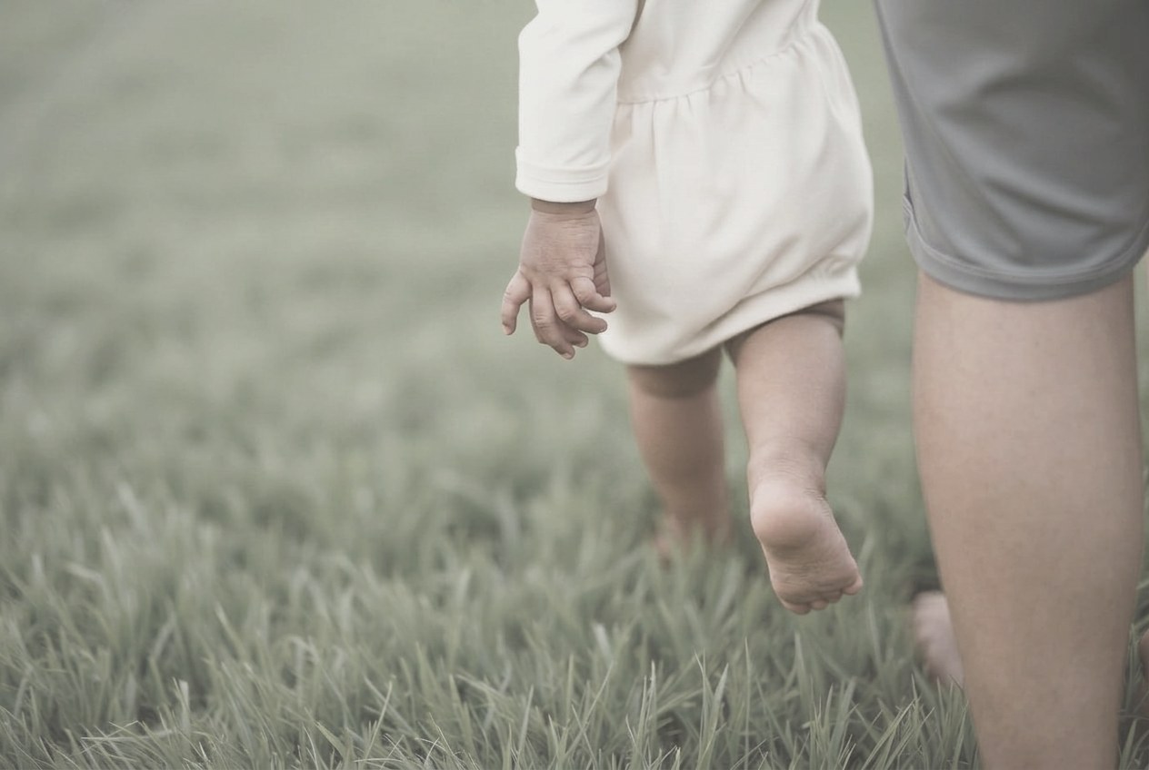 A small child’s hand held in an adult’s hand on the grass
