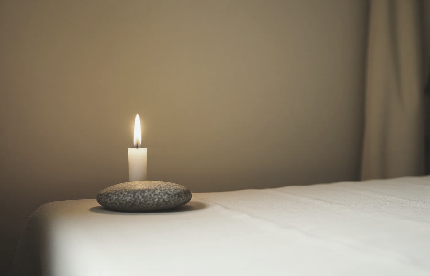 A single candle flame beside a smooth stone in a quiet room