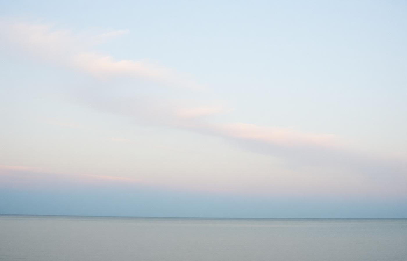A wide pale sky of slow clouds above still water